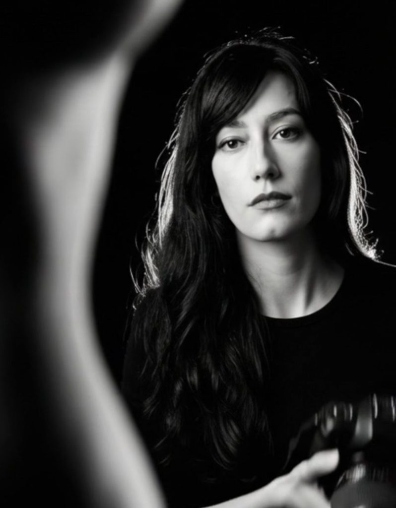 A female photographer is analysing a scene while holding a professional camera in her hands.